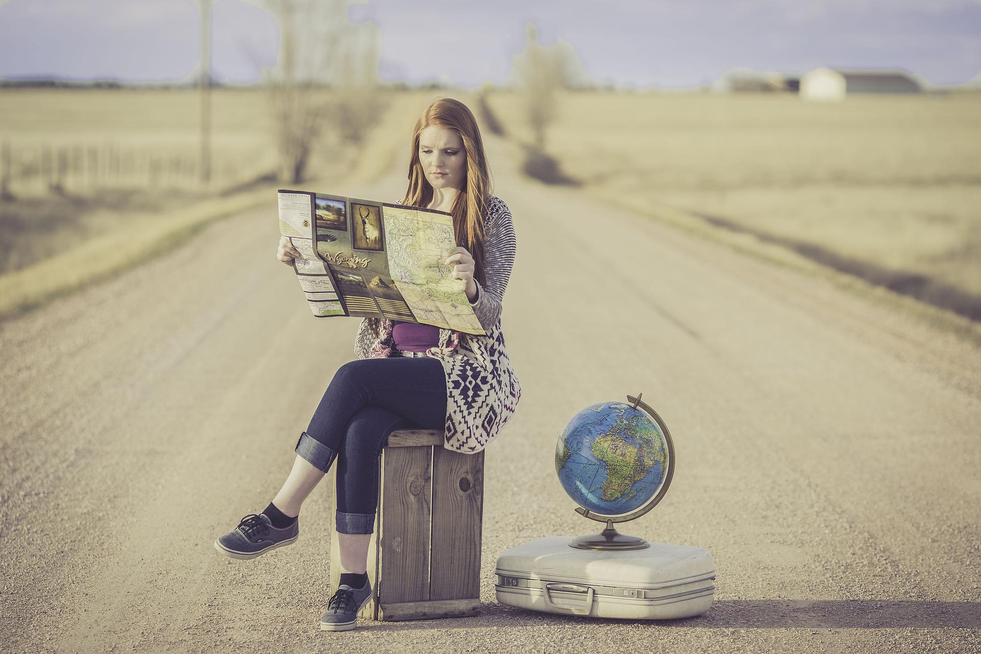 道でスーツケースに座り地図を見ている女性
